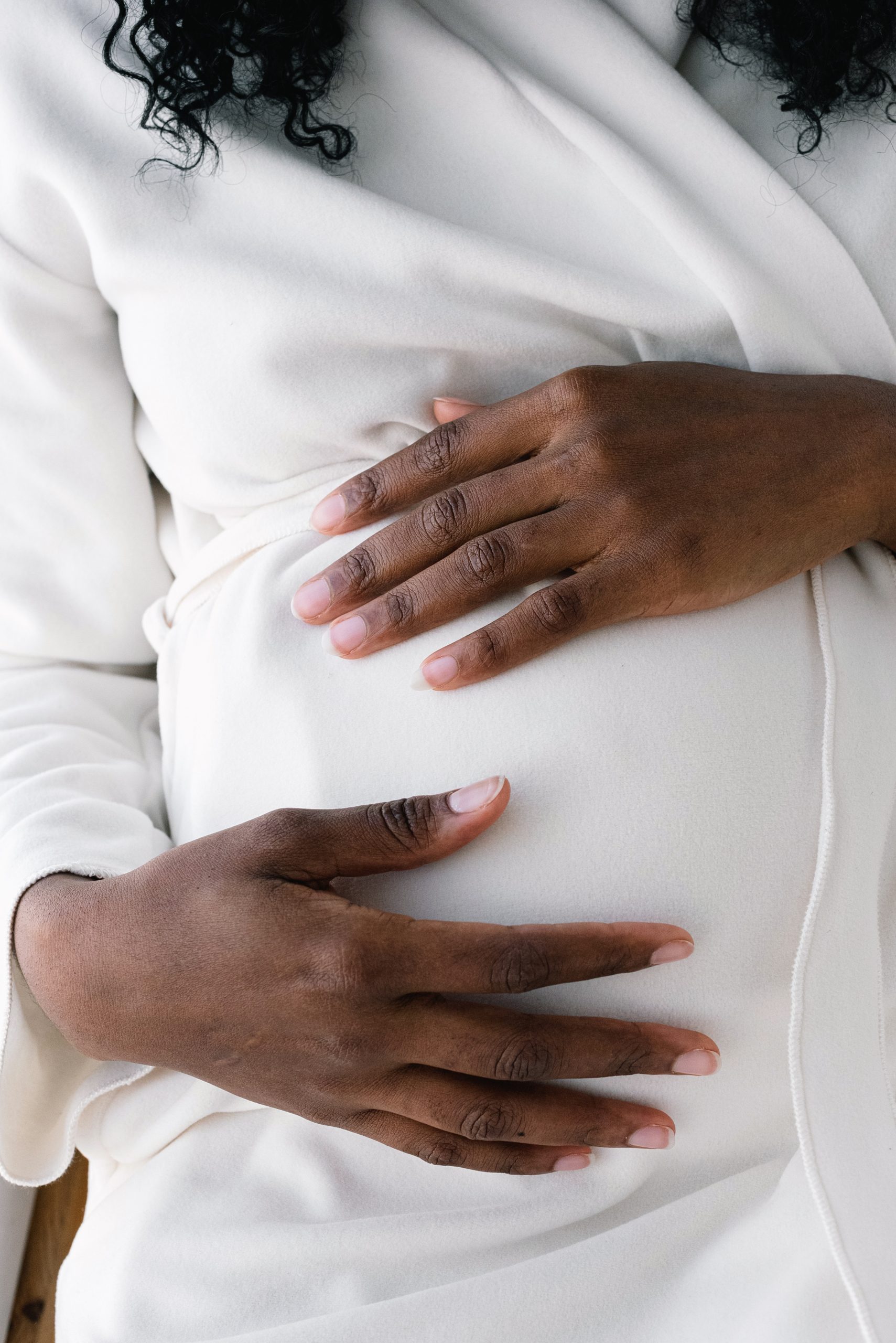 A pregnant woman in white cradling her belly with both hands.