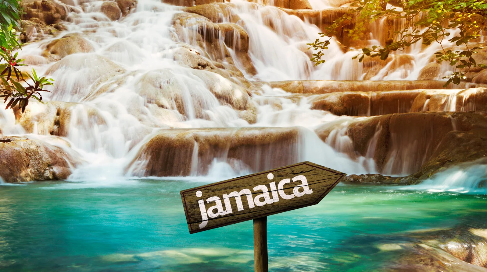 A waterfall cascading over rocks into turquoise water in Jamaica, with a wooden signpost reading "jamaica".